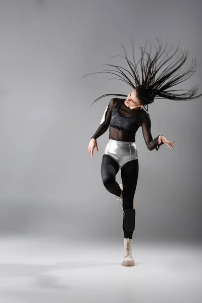 Longitud completa de la mujer expresiva de estilo futurista con trenzas posando sobre fondo gris - foto de stock