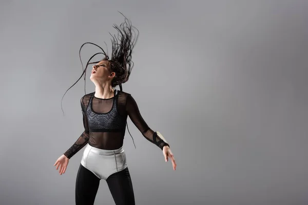 Fit woman in futuristic bodycon jumpsuit and silver shorts posing with dreadlocks on wind isolated on grey — Stock Photo