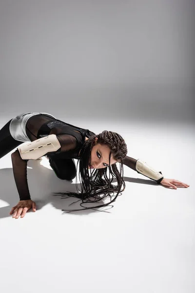 Expressive woman in futuristic outfit and dreadlocks looking at camera while posing on grey background — Stock Photo