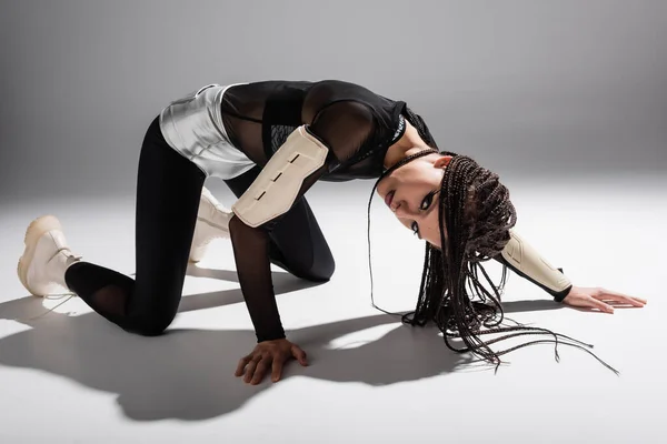 Expressive woman with dreadlocks posing in futuristic outfit and looking at camera on grey background — Stock Photo