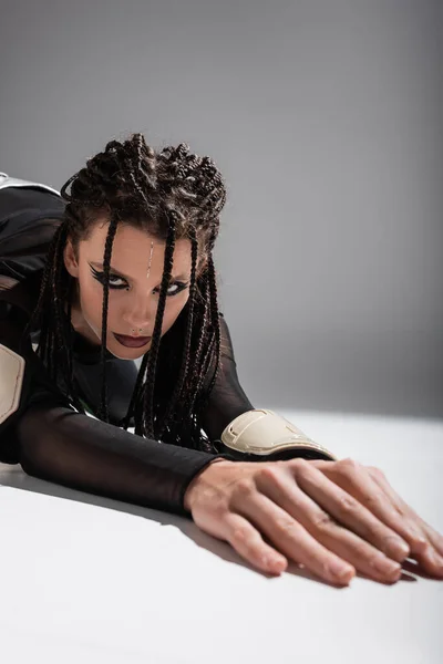 Brunette woman with futuristic makeup and dreadlocks posing on white surface and grey background — Stock Photo