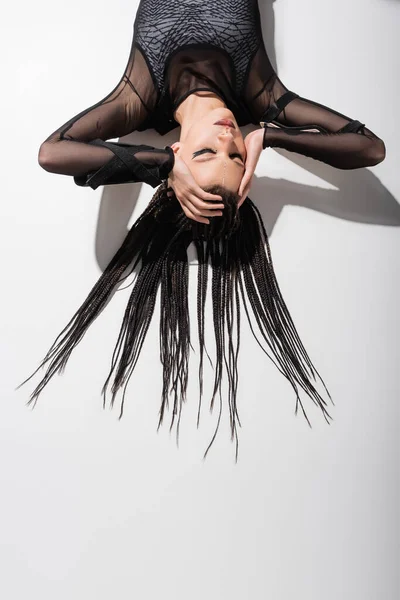 Vista superior de la mujer futurista con trenzas tocando la cabeza mientras está acostado sobre fondo blanco con sombra — Stock Photo