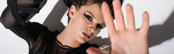 Draufsicht der Frau mit ausdrucksstarkem Make-up und ausgestreckter Hand, die in die Kamera auf weißem Hintergrund mit Schatten blickt, Banner — Stockfoto
