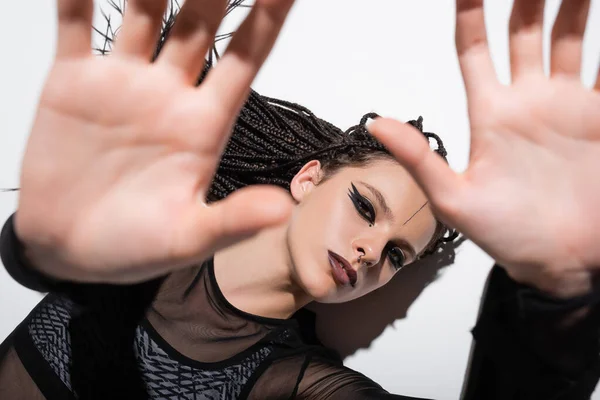 Vista superior de la mujer con maquillaje elegante acostado con las manos extendidas borrosas sobre fondo blanco con sombra - foto de stock