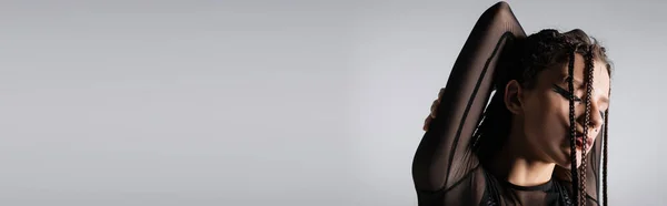 Брюнетка жінка з макіяжем і косами позує із закритими очима і руками за голову ізольована на сірому, банер — стокове фото