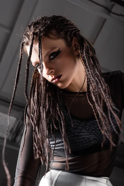 Low angle view of futuristic style woman with stylish makeup and dreadlocks on grey background — Stock Photo