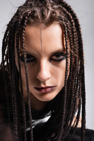 Porträt einer jungen Frau mit futuristischem Make-up und Dreadlocks, die isoliert auf grau in die Kamera blickt — Stockfoto