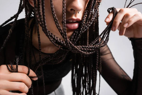 Cropped view of woman with piercing touching braided dreadlocks isolated on grey — Stock Photo