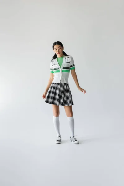 Full length of young asian woman in skirt and knee socks standing on grey background — Stock Photo