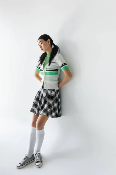 Joven mujer asiática en zapatillas de deporte y falda de pie sobre fondo gris — Stock Photo