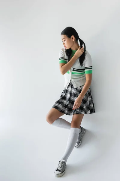 Pleine longueur de jeune asiatique femme dans recadré cardigan et jupe debout sur gris fond — Photo de stock