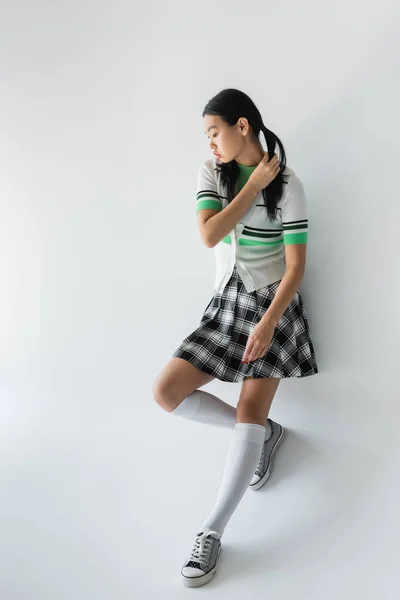 Full length of young asian woman in cropped cardigan and skirt standing on grey background — Stock Photo