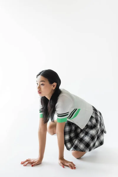 Stylish asian model kneeling and looking away on grey background — Stock Photo