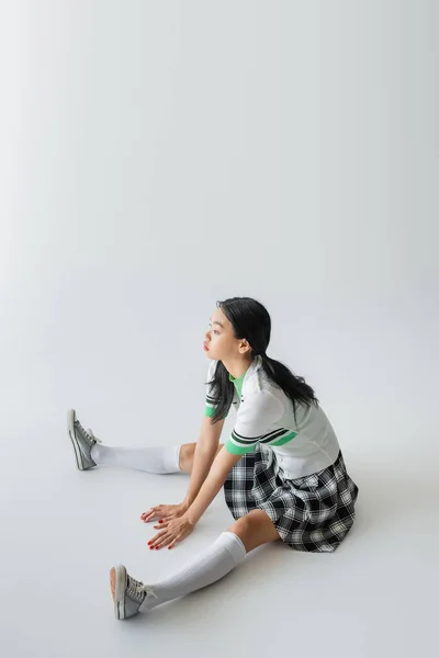 Elegante mujer asiática en falda y calcetines de rodilla sentado sobre fondo gris — Stock Photo