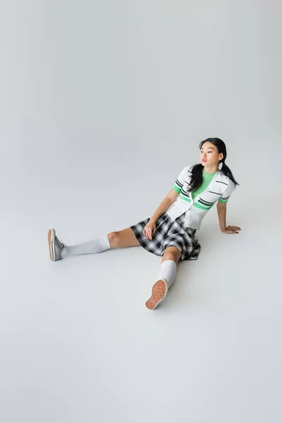 Stylish asian model in knee socks and sneakers sitting on grey background — Stock Photo