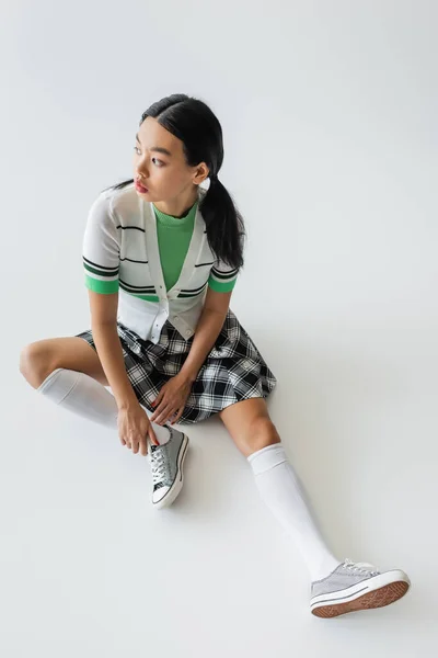 High angle view of pretty asian woman in sneakers and knee socks sitting on grey background — Stock Photo
