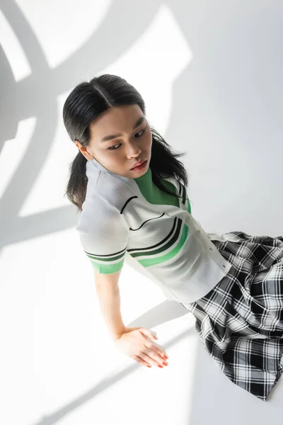 High angle view of stylish asian model sitting on grey background with light — Stock Photo