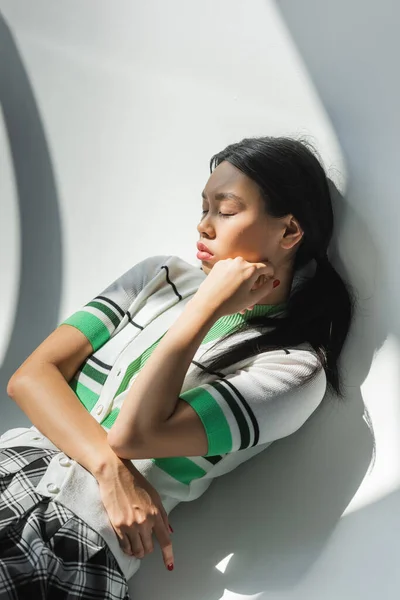 Elegante modelo asiático em cardigan cortado posando com olhos fechados no fundo cinza — Fotografia de Stock