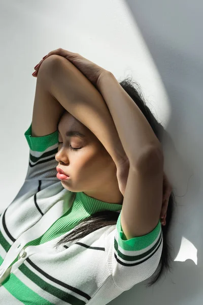 High angle view of young asian woman in cropped cardigan lying on grey background with light — Stock Photo
