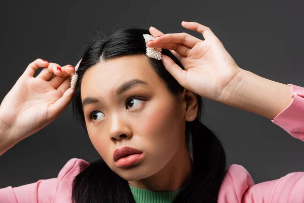 Pretty asian model touching barrettes and looking away isolated on grey — Stock Photo