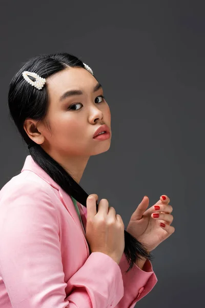 Porträt einer asiatischen Frau in rosa Jacke, die ihr Haar isoliert auf grau berührt — Stockfoto