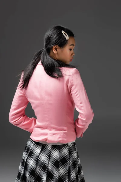 Side view of fashionable asian woman in plaid skirt and pink jacket isolated on grey — Stock Photo