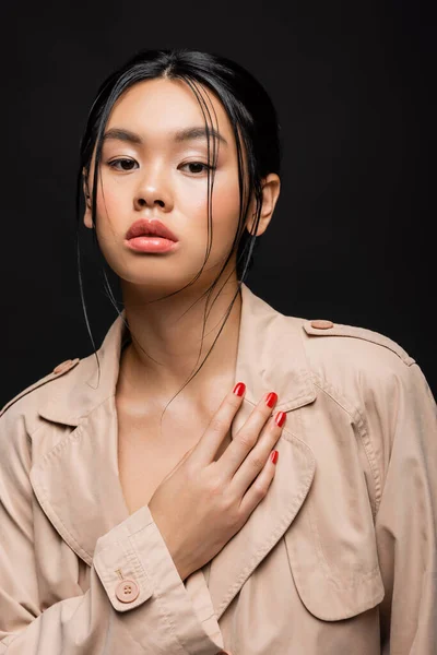 Retrato de elegante modelo asiático en gabardina beige aislado en negro - foto de stock