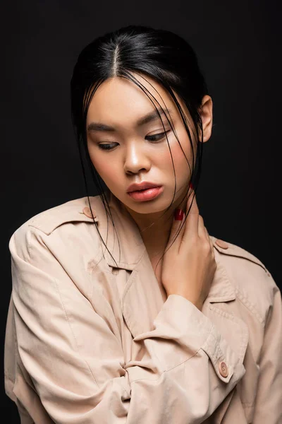 Portrait de joli modèle asiatique en trench coat beige regardant loin isolé sur noir — Photo de stock