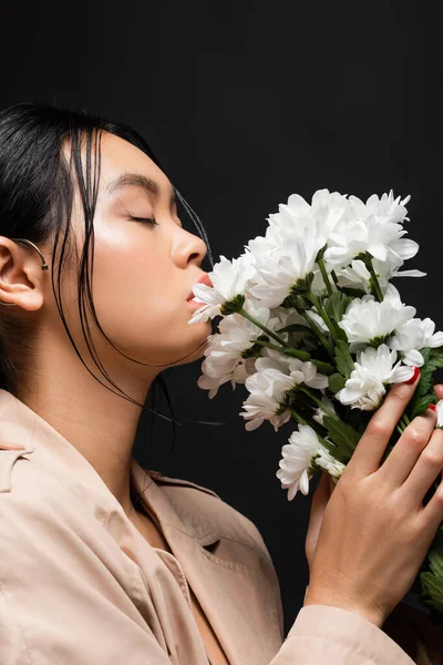 Portrait of asian woman in beige trench coat holding white flowers isolated on black — Stock Photo