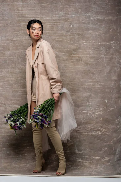 Lunghezza completa del modello asiatico in trench contenente fiori con stoffa su sfondo marrone astratto — Foto stock