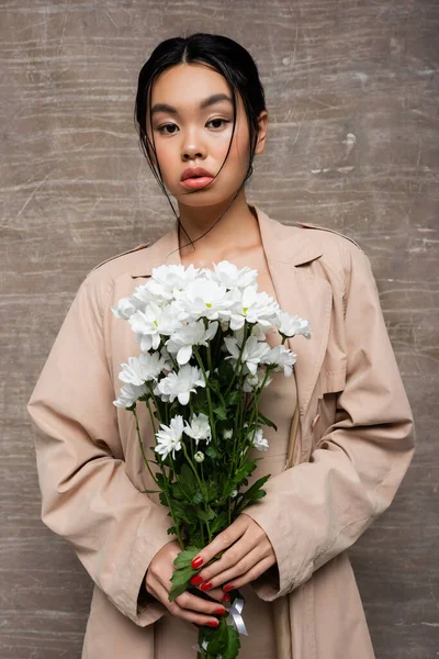 Portrait of asian woman holding chrysanthemums on abstract brown background — Stock Photo