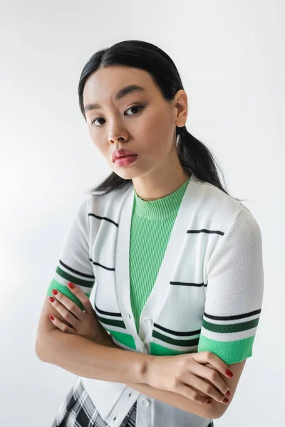 Portrait of asian model in cropped cardigan crossing arms isolated on grey — Stock Photo