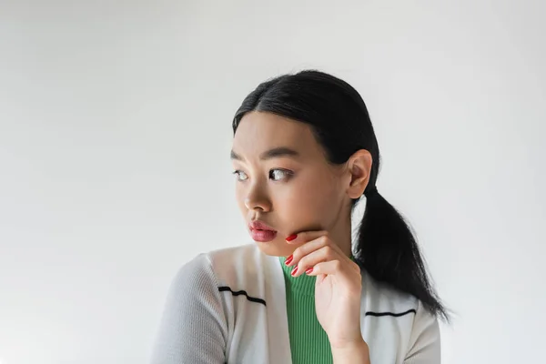Retrato de modelo asiático bonito con manicura roja mirando hacia otro lado aislado en gris - foto de stock
