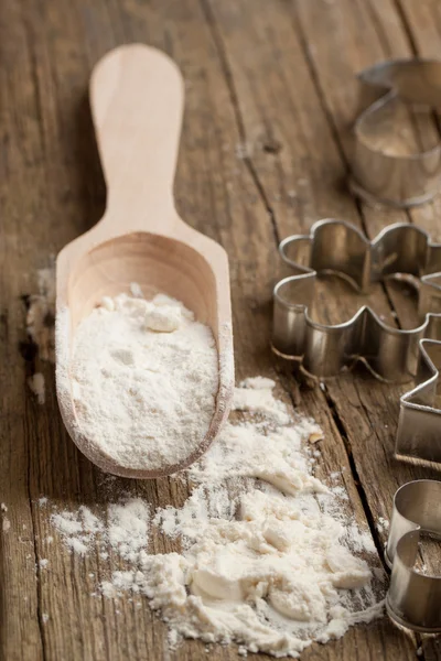 Wooden spoon with flour and cookie cutters — Stock Photo, Image