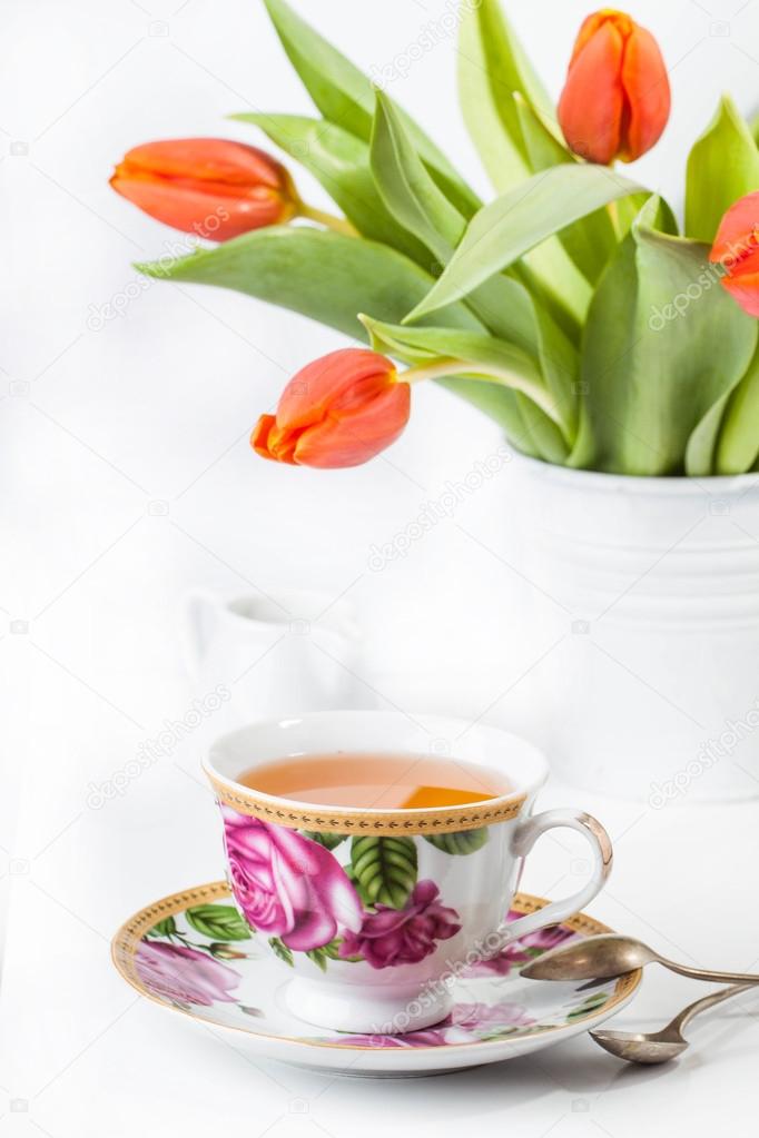 Cup of tea with red tulips over white