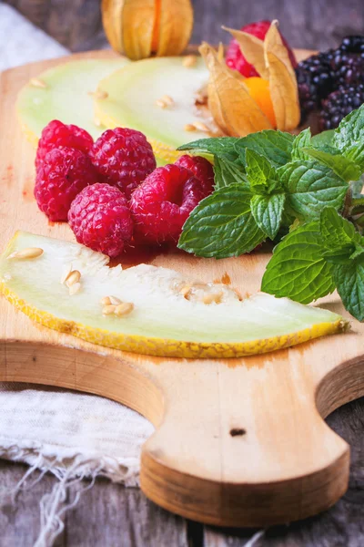 Bayas, menta y melón sobre tabla de cortar de madera — Foto de Stock