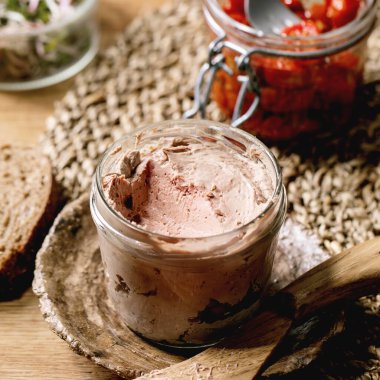 Cam kavanoz ev yapımı tavuk ciğeri dilimlenmiş çavdar ekmeği, güneşte kurutulmuş domates ve ahşap mutfak masasında yeşil lahana salatası. Ev kahvaltısı ya da aperatif. Kare resim