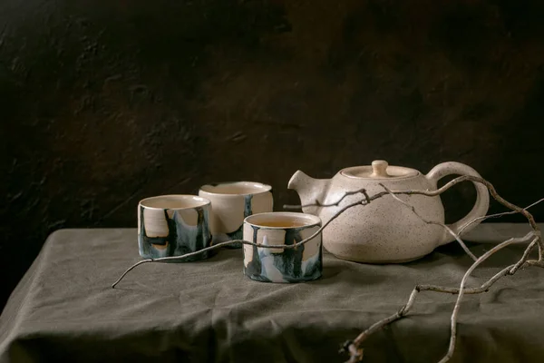 在黑暗的房间里 手工制作的白色茶壶茶壶 茶壶上有一杯热茶 用于茶道仪式 放在亚麻桌布上 — 图库照片