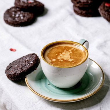 Kurutulmuş ahududu, tuzlu gevrek ve beyaz pamuk masa örtüsünün üzerinde kahve espresso ile süslenmiş ev yapımı çikolatalı browni kurabiyeleri. Kare resim