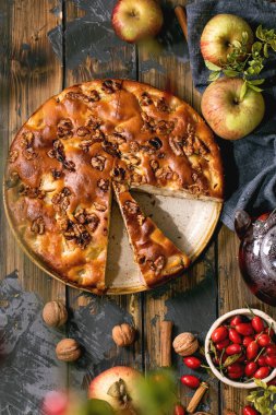 Ev yapımı elma ve cevizli kek Charlotte tabakta taze elma, fındık, koyu ahşap arka planda gül kalçası çayı. Sonbahar sıcacık pişirme. Düz yatıyordu
