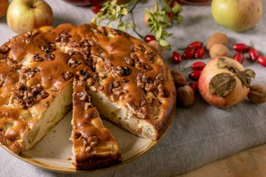 Ev yapımı elma ve cevizli kek Charlotte tabakta taze elmalar, tarçınlı ve fındıklı gri keten masa örtüsü. Sonbahar ev yapımı, kapat.