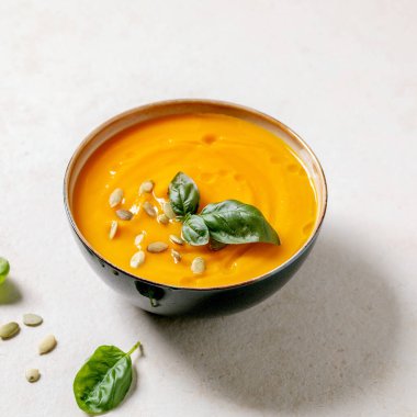 Bir kase balkabağı ya da taze fesleğen, zeytin yağı ve kabak tohumlarıyla süslenmiş havuçlu vejetaryen kremalı çorba. Kare resim