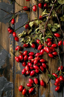 Ağaç dallı gül kalçası böğürtlenleri ve eski koyu ahşap arka planda yapraklar. Kış için sonbahar vitamin rezervleri. Düz yat, boşluğu kopyala