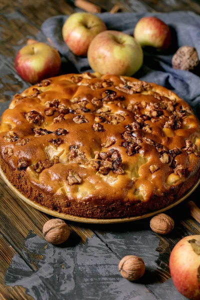 Ev yapımı elma ve cevizli kek Charlotte tabakta taze elma, tarçın ve fındıklı koyu ahşap masa. Sonbahar ev yapımı..