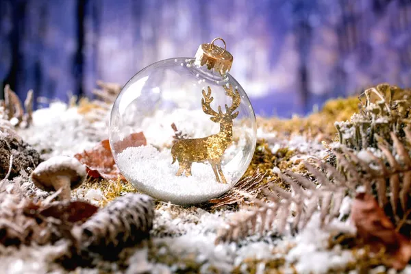 クリスマスや新年の挨拶カード 冬の森を背景に雪に覆われた苔の上にガラス透明玉の黄金の鹿 クリスマス休暇の雰囲気 — ストック写真