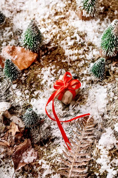 クリスマスや新年の挨拶カード 赤いリボン弓 雪に覆われた苔の周りの小さな装飾クリスマスツリーとクラフト紙のギフトボックス クリスマス休暇の雰囲気 高角度表示 — ストック写真