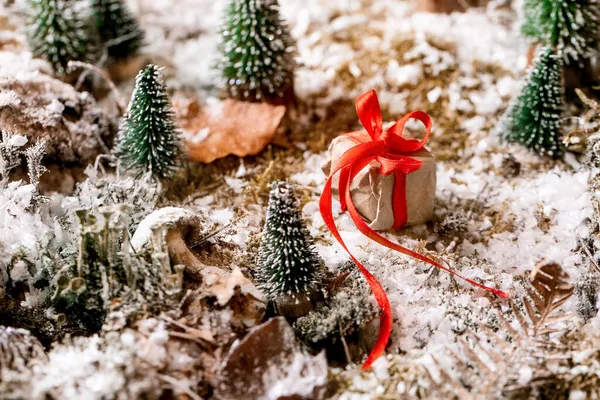 クリスマスや新年の挨拶カード 赤いリボンとクラフト紙のギフトボックス 凍結された雪の覆われた苔の周りの小さな装飾的なクリスマスツリー クリスマス休暇の雰囲気 高角度表示 — ストック写真