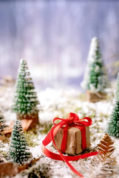 クリスマスや新年の挨拶カード 赤いリボンが付いたクラフト紙のギフトボックス 冬の森を背景に雪に覆われた苔の周りの装飾的なクリスマスツリー クリスマス休暇の雰囲気 — ストック写真