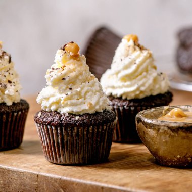 Beyaz krem şantili ev yapımı çikolatalı kekler ve ahşap masadaki seramik tabakta tuzlu karamel. Kare resim