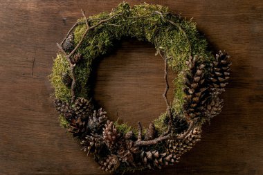 El yapımı DIY Noel tatili çelenkleri doğal orman yosunları ve ahşap arka planda koniler..
